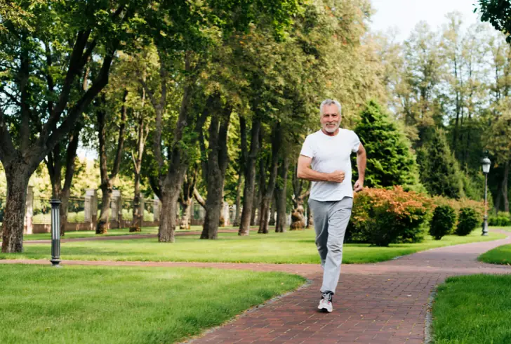 Older man jogging through green park